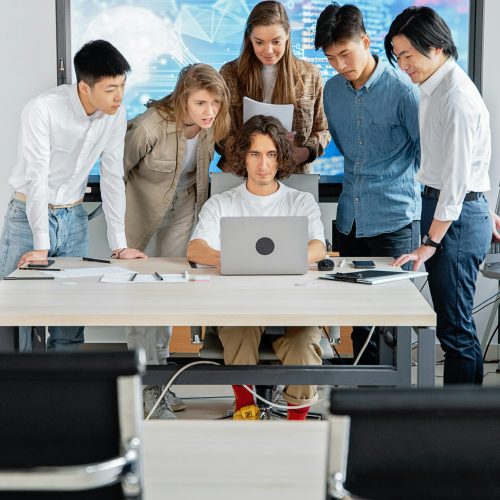 A diverse group of professionals engaged in teamwork around a laptop in a contemporary office setting.